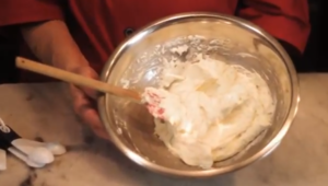 A bowl of smooth buttermilk frosting being whipped to a creamy consistency, perfect for cakes and cupcakes, with ingredients like butter, brown sugar, and powdered sugar in the background.