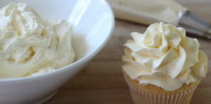 This image shows a freshly whipped batch of buttermilk frosting, smooth and creamy in texture, ready to be spread on cakes or cupcakes. Surrounding the bowl are key ingredients like butter, brown sugar, powdered sugar, and a whisk, highlighting the simplicity of the recipe.