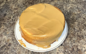 Smooth caramel frosting being spread on a cake with a spatula.