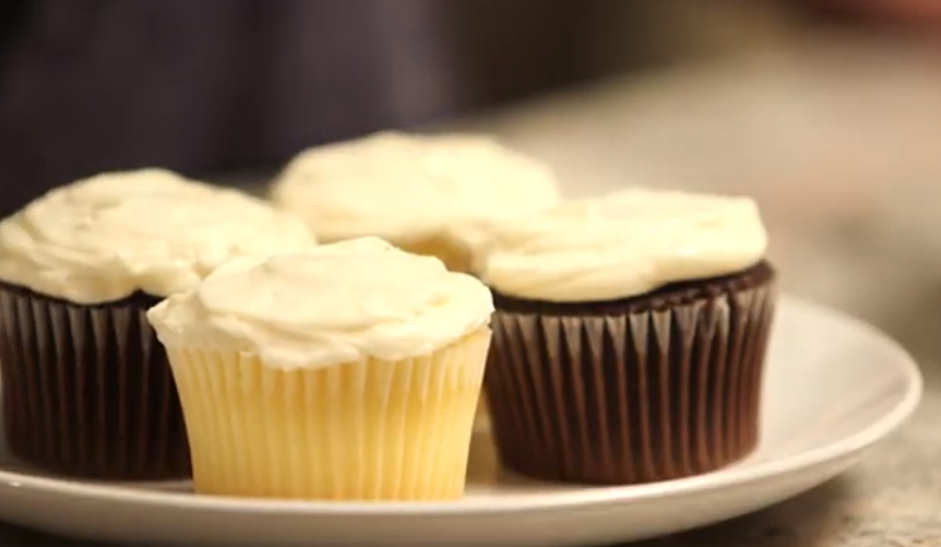 A bowl of smooth buttermilk frosting being whipped to a creamy consistency, perfect for cakes and cupcakes, with ingredients like butter, brown sugar, and powdered sugar in the background