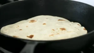 Freshly made homemade tortillas stacked on a wooden table.