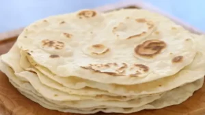 Freshly made homemade tortillas stacked on a wooden table.