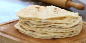 Freshly made homemade tortillas stacked on a wooden table.