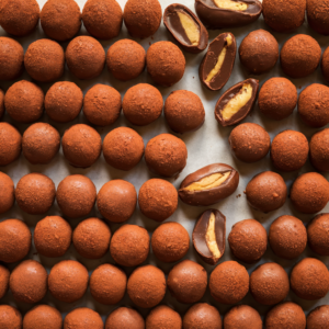 Chocolate-covered peanuts on a tray, coated with rich cocoa powder, showing a deliciously smooth and glossy chocolate coating.