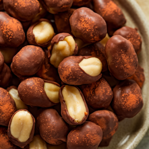 Chocolate-covered peanuts on a tray, coated with rich cocoa powder, showing a deliciously smooth and glossy chocolate coating.