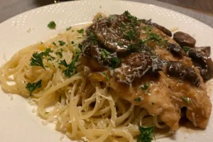 Fried chicken topped with creamy mushroom sauce served over spaghetti, garnished with parsley and grated cheese on a white plate.