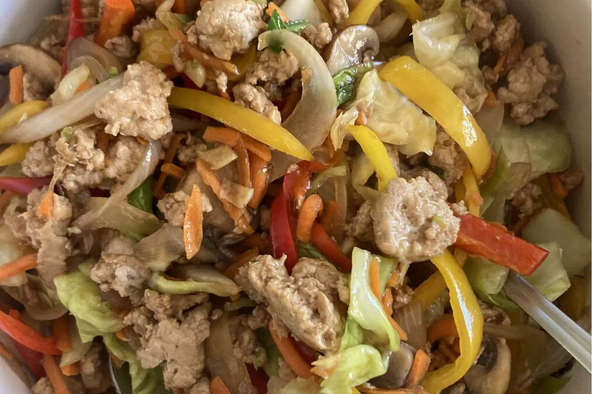 A close-up of a turkey and vegetable stir-fry, showing ground turkey, bell peppers, onions, carrots, cabbage, and mushrooms mixed together in a vibrant, healthy dish.